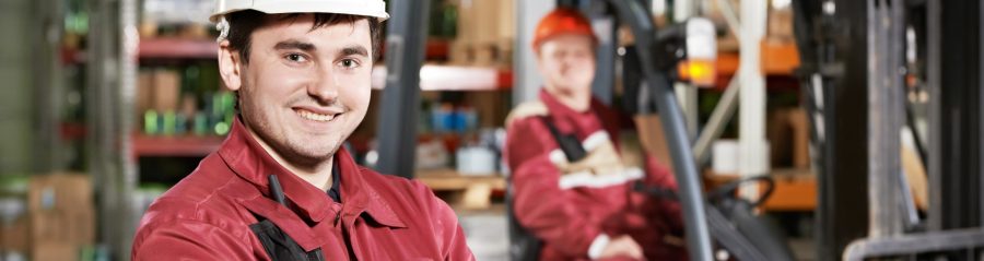 young smiling warehouse worker driver in uniform in front of forklift stacker loader