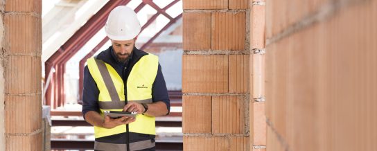 Man with safety helmet touching bare brick wall
