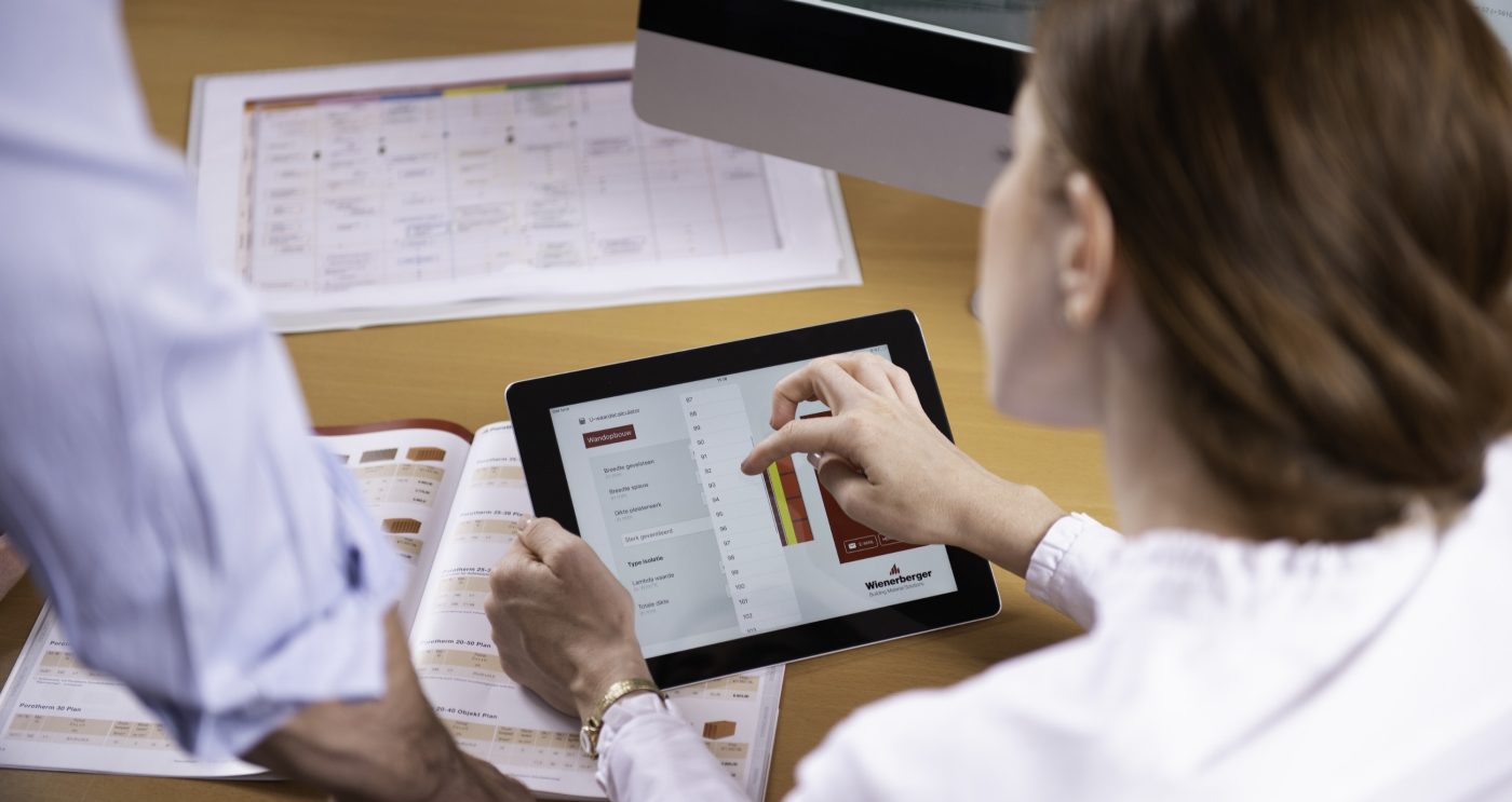 Woman at workplace holding tablet computer sitting next to standing man