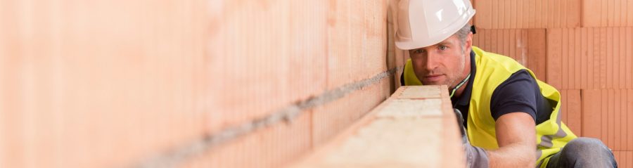 Construction worker checking alignment of mineral-wool filled clay block