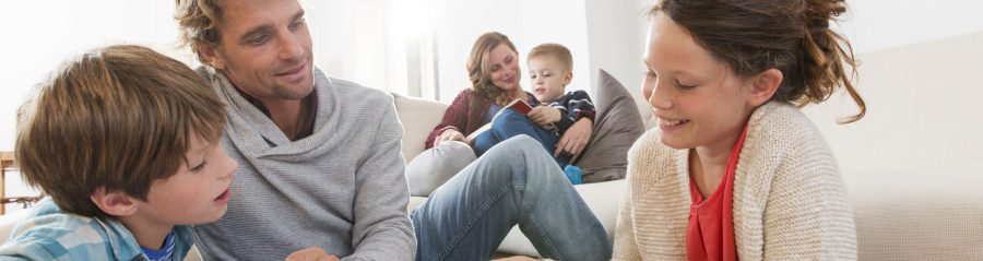 Father with two kids sketching and mother with boy reading a book in living room