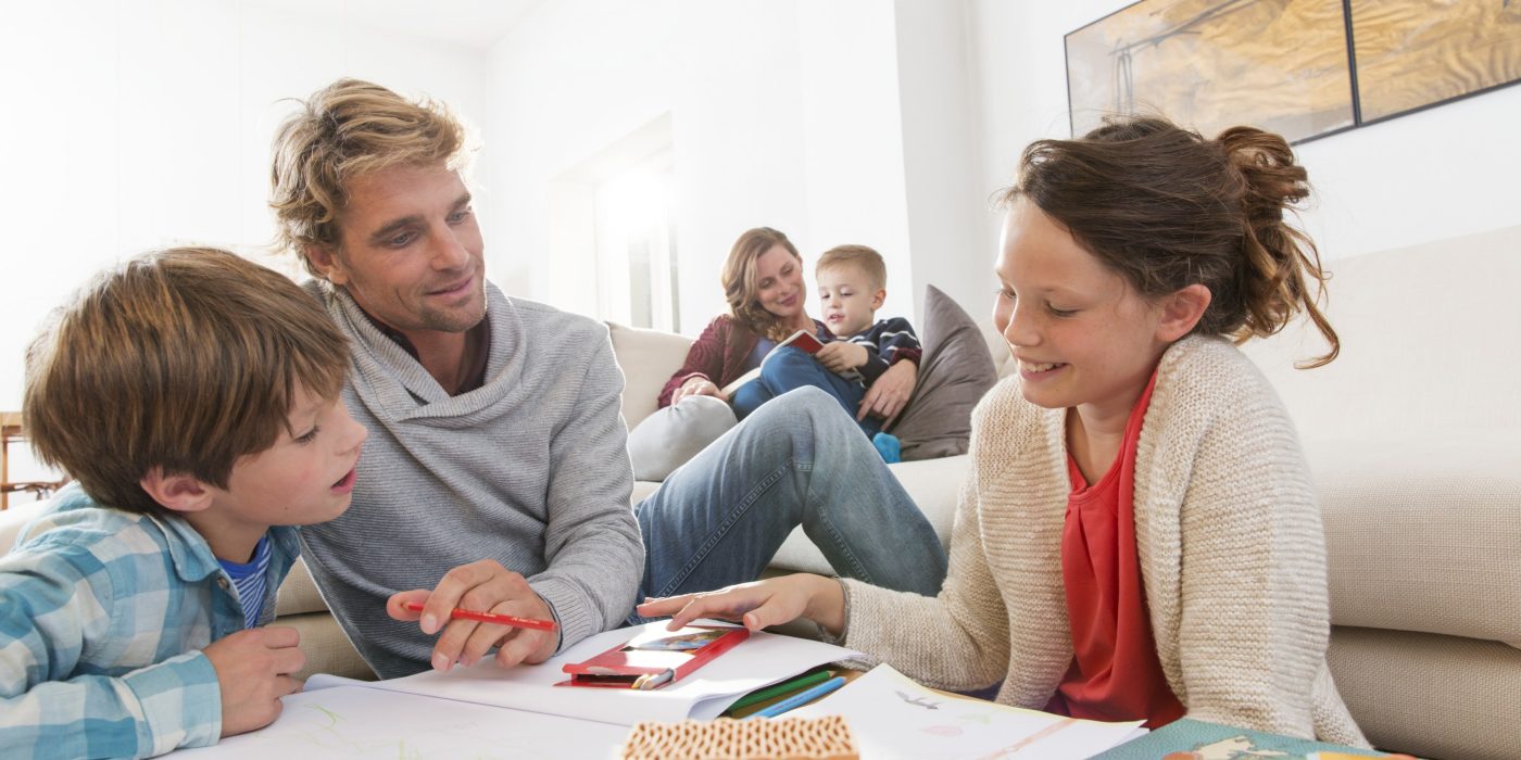 Father with two kids sketching and mother with boy reading a book in living room