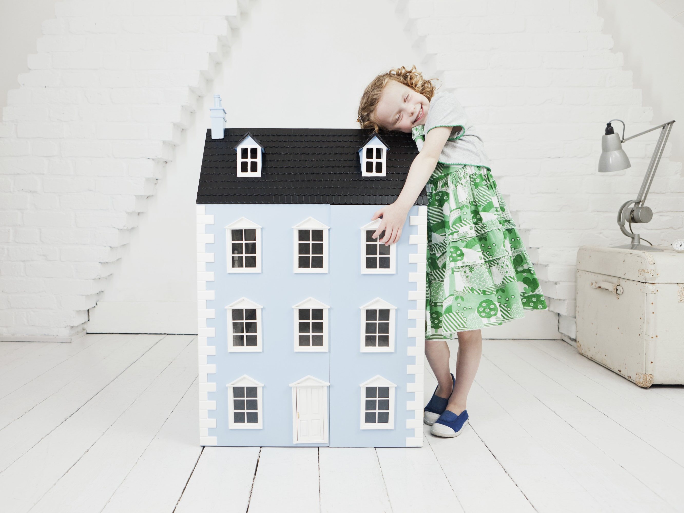 Happy girl leaning against doll house in attic loft
