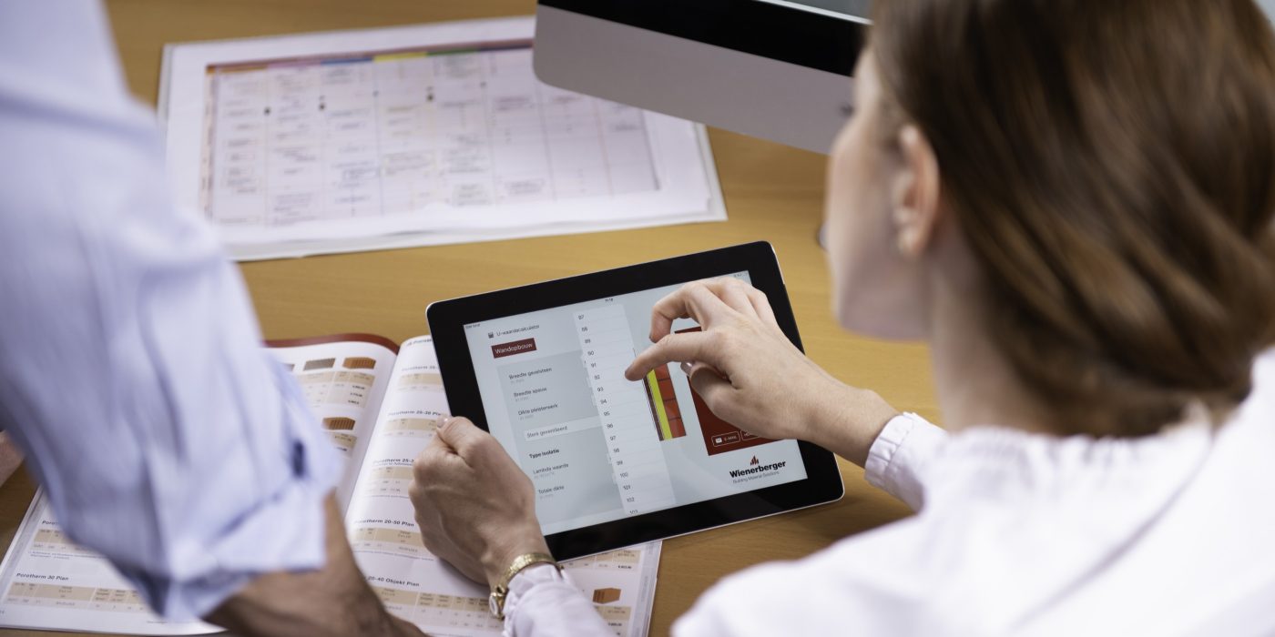 Woman at workplace holding tablet computer sitting next to standing man