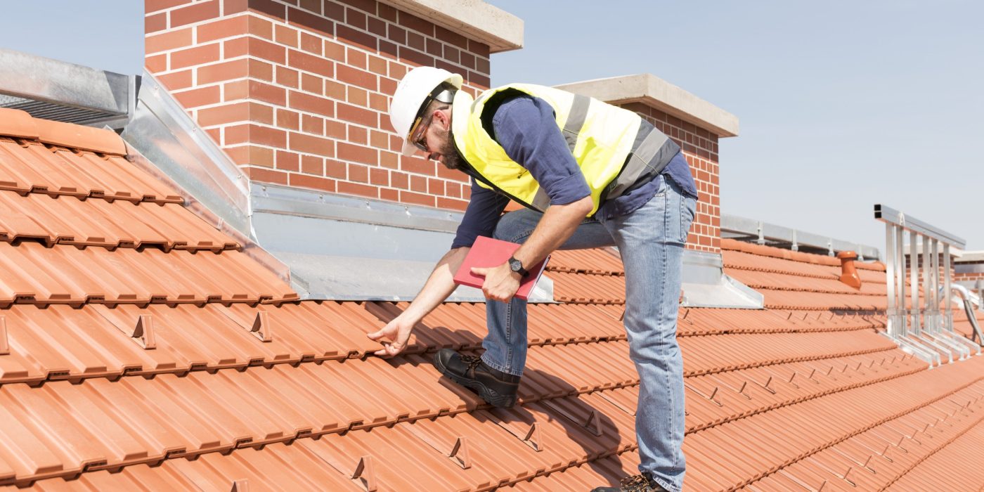 Product manager checking ventilation roof tiles in front of chimney standing on the roof wearing hard hat and safety jacket