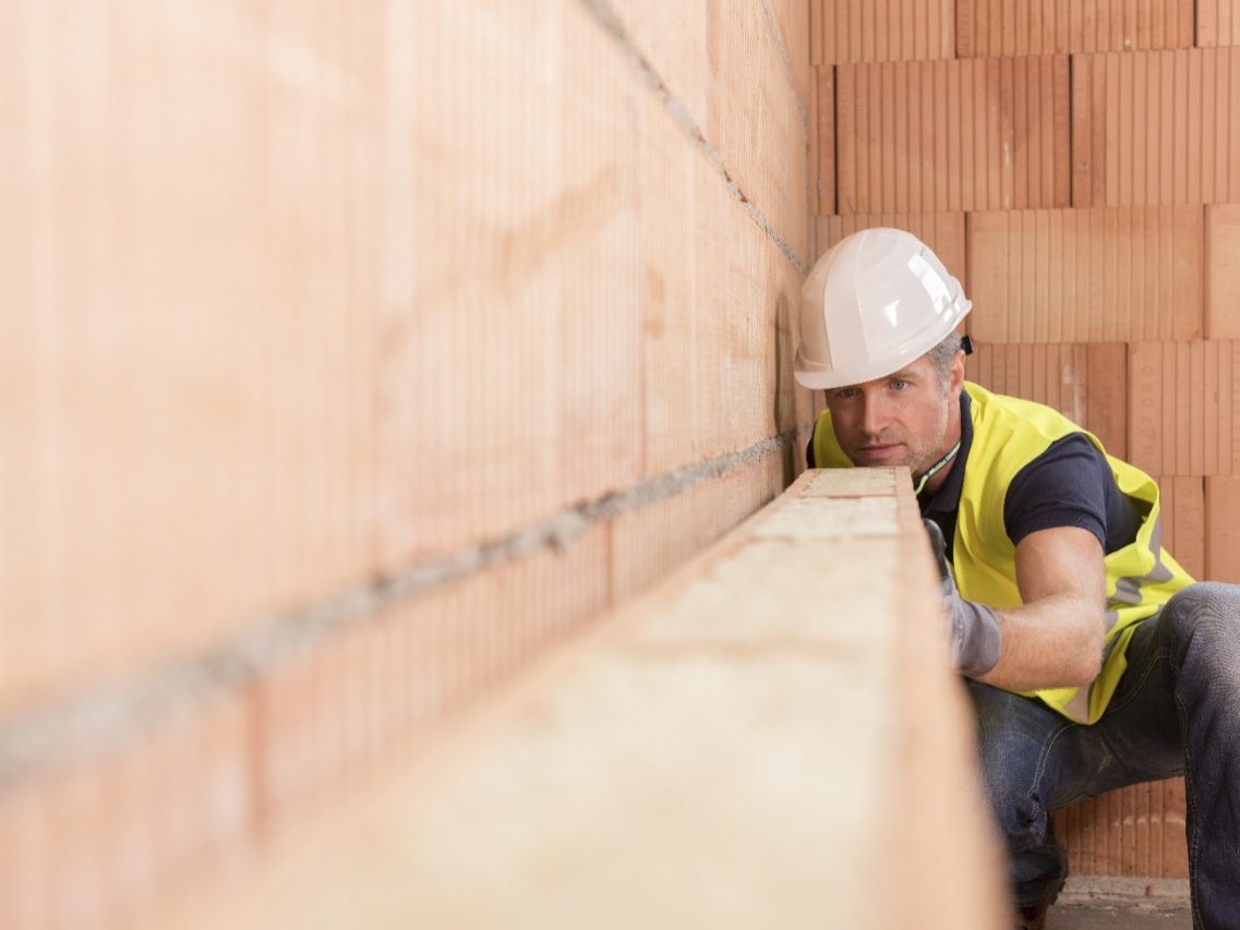 Construction worker checking alignment of mineral-wool filled clay block