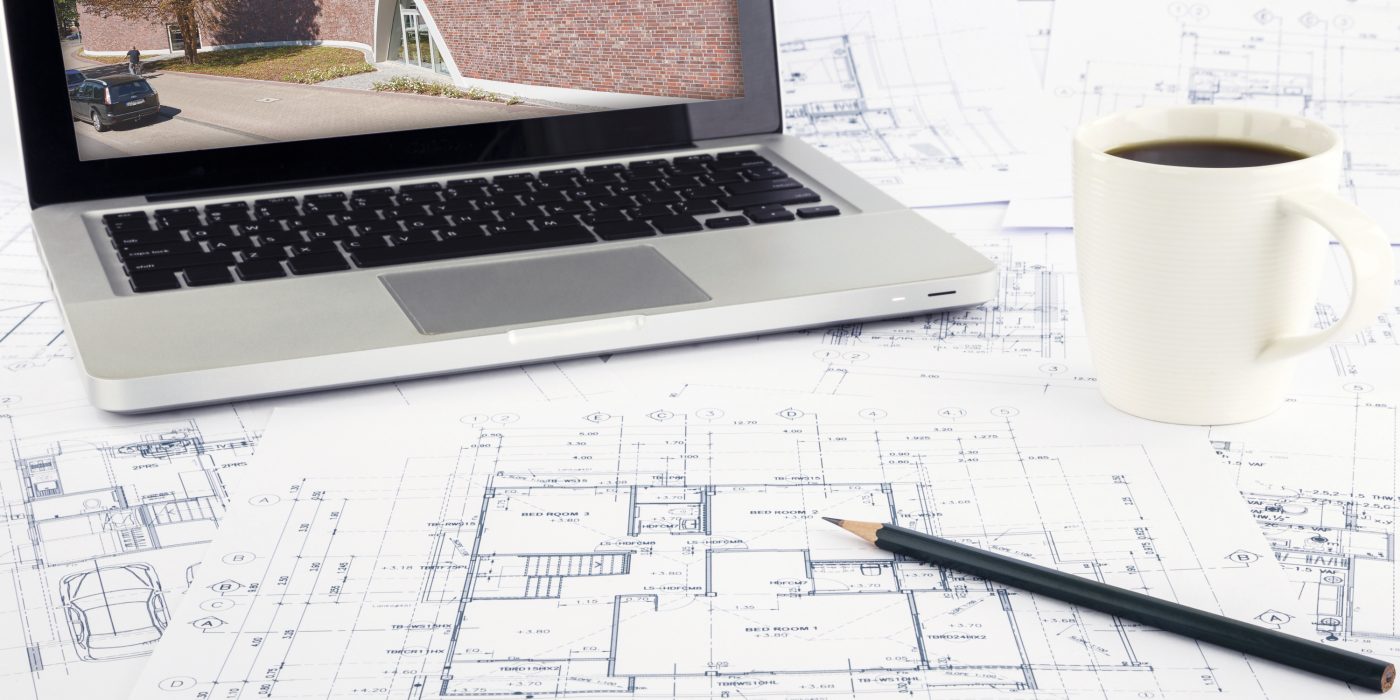 Working space with reference picture on laptop and architecture plan on desk