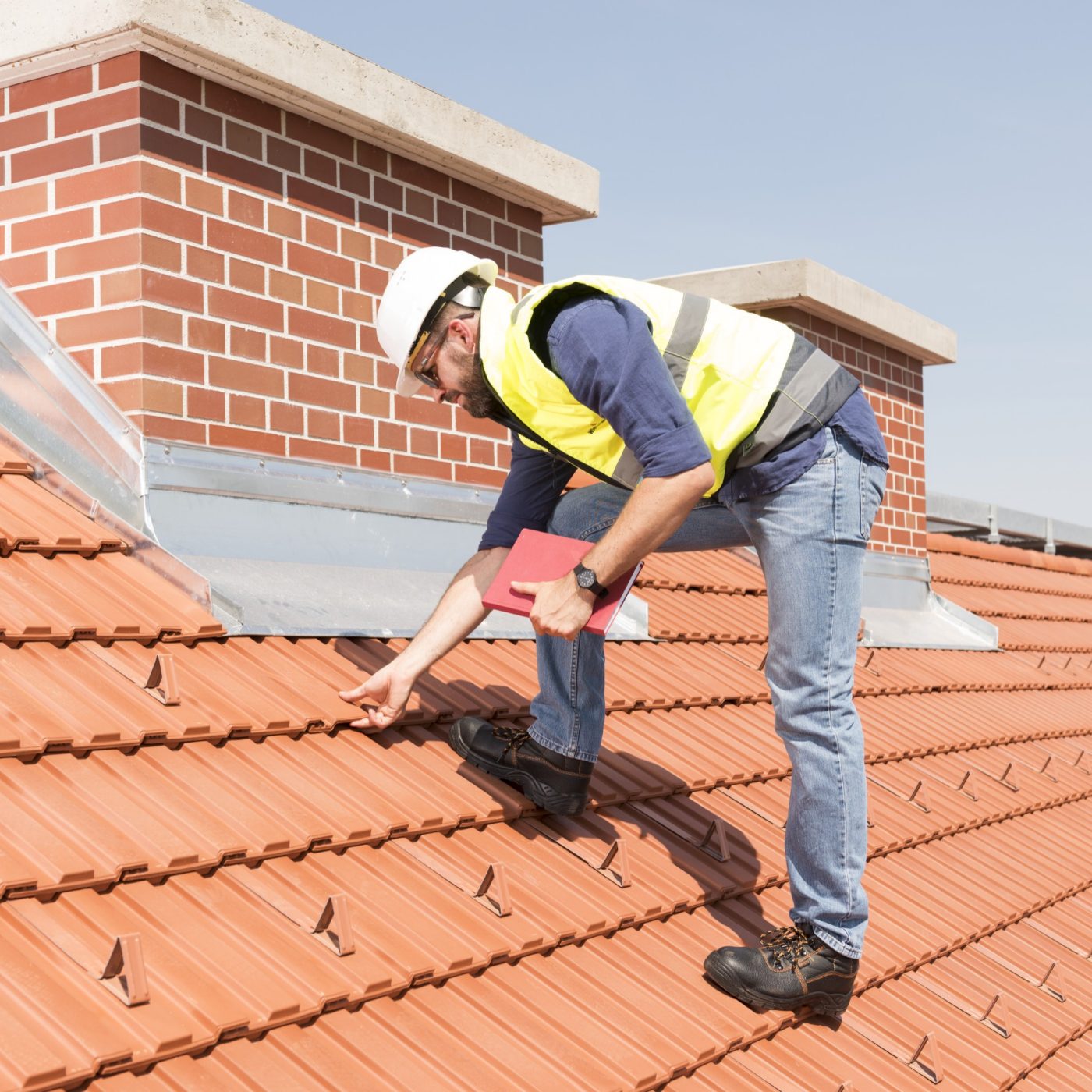 Product manager checking ventilation roof tiles in front of chimney standing on the roof wearing hard hat and safety jacket