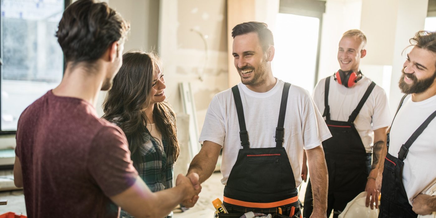Happy manual worker welcoming young couple to their renovated apartment.