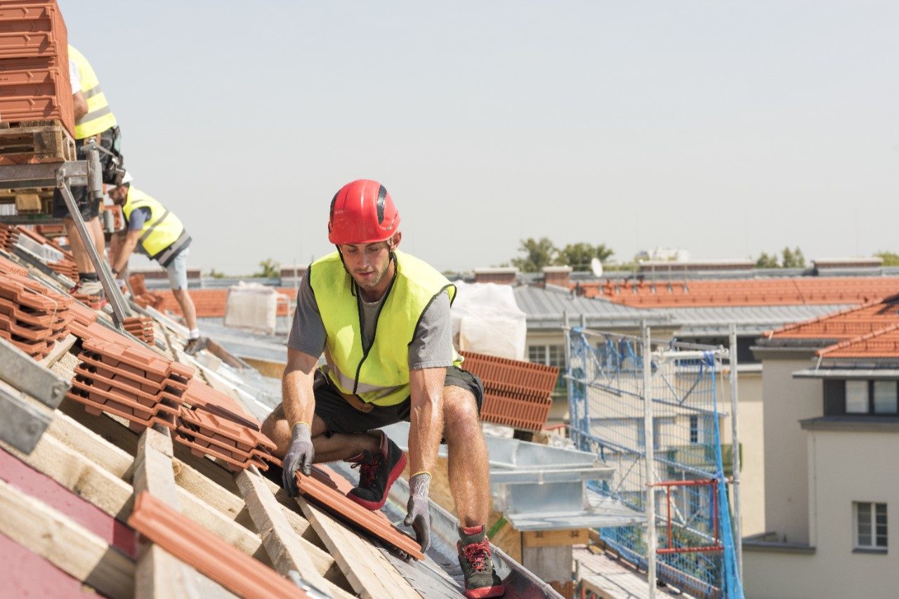 Urban roofers at work wearing safety jacket and hard hat laying roof tiles at an urban location