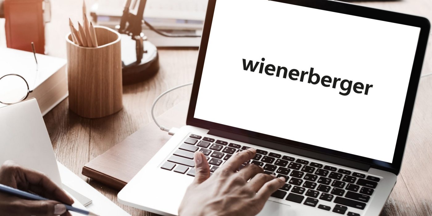 Someone typing on a laptop, pencil and notebook, Wienerberger logo on the screen