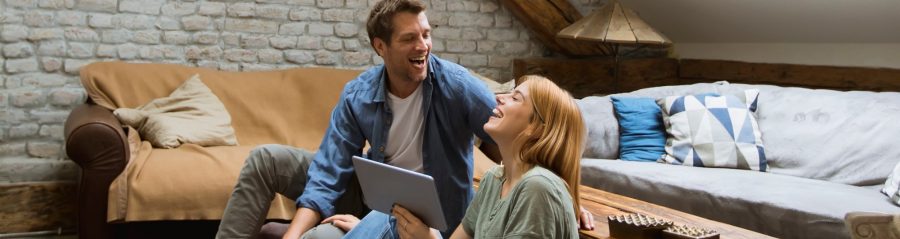 Happy young couple using tablet sitting on the floor at home